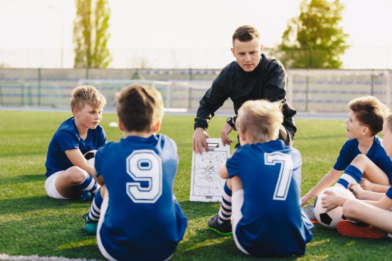 Young coach teaching kids on football field.