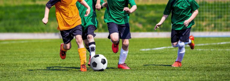 Running Youth Football Players. Kids Playing Football Soccer Game on Sports Field. Boys Play Soccer Match on Green Grass. Youth Soccer Tournament Teams Competition.